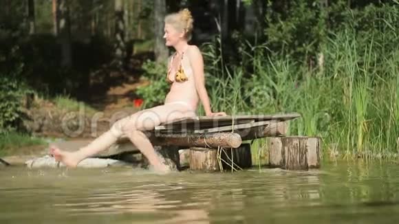 一个漂亮的女人坐在湖边的木墩上放松视频的预览图