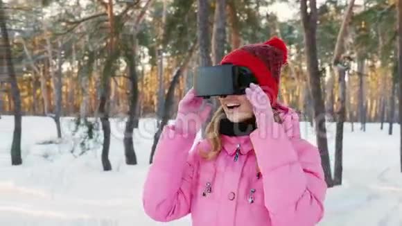 戴着虚拟现实眼镜的年轻女子在白雪覆盖的森林里环顾四周捕捉雪花冬天的乐趣视频的预览图