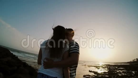 男人和女人站在海边拥抱和亲吻日落日落海滩上的情侣视频的预览图
