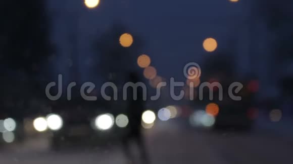 晚上在城里行人剪影穿过街道汽车前灯模糊挡风玻璃上有水滴夜晚的城市视频的预览图