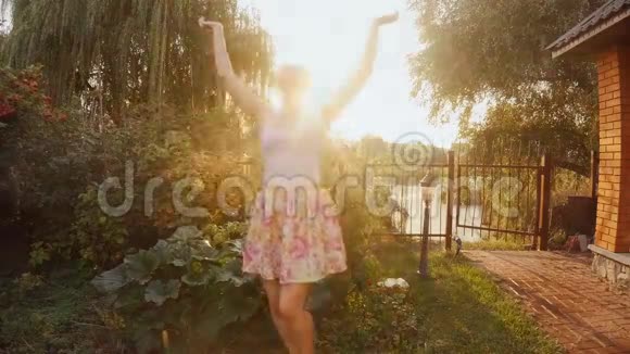 美丽的年轻女子在花园的水滴下跳舞的慢镜头视频的预览图