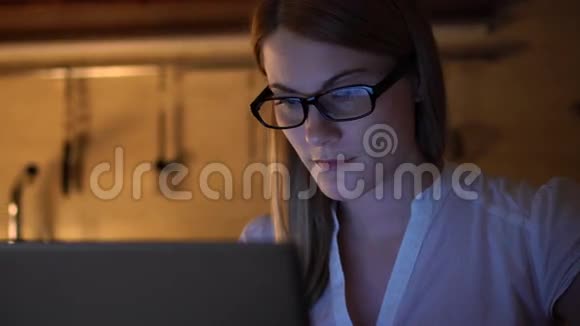漂亮迷人的女人戴着眼镜在笔记本电脑上浏览互联网晚上厨房喝咖啡视频的预览图