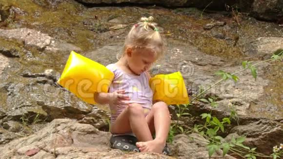 手臂上的小金发女孩在石头上的腿视频的预览图