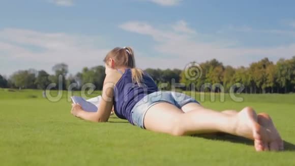 在公园草地上用双腿读书的漂亮女孩的多莉照片视频的预览图