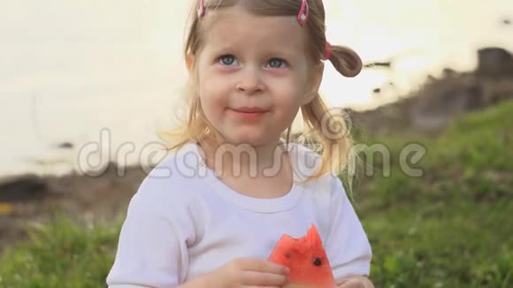 小可爱的小女孩吃红西瓜坐在池塘边的绿草上视频的预览图