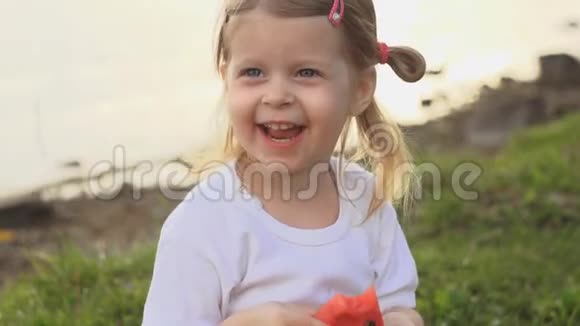 小可爱的小女孩吃红西瓜坐在池塘边的绿草上视频的预览图