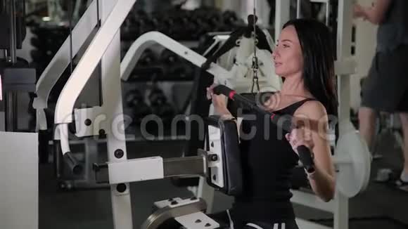 漂亮的运动年轻女孩在健身房里对胸部模拟器进行拉力视频的预览图