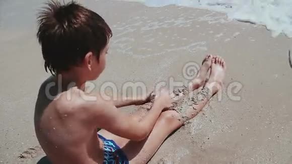 男孩9岁坐在海边的沙滩上玩海沙浪淘沙洗孩子脚视频的预览图