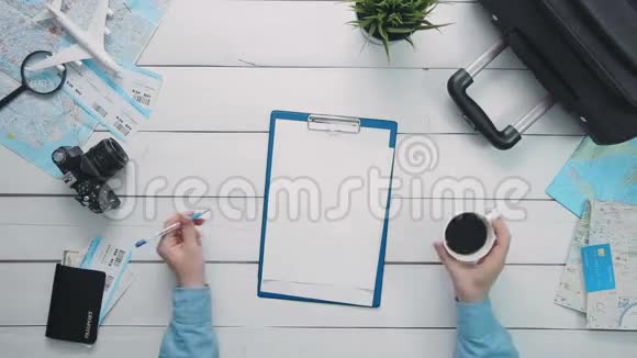 在白色的木桌上顶景旅行者手拿着笔一杯咖啡和一个夹纸板视频的预览图