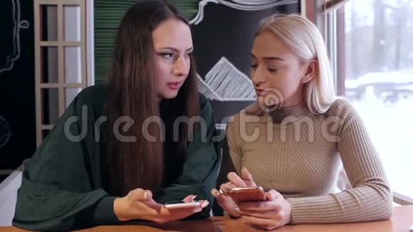 两个年轻女孩坐在一家带电话的咖啡馆里视频的预览图