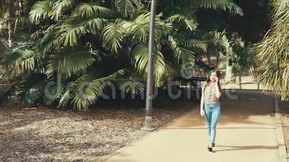 女孩走在城市棕榈公园通过电话交谈阳光明媚视频的预览图