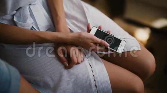 年轻女性穿着浴袍使用智能手机的特写镜头女性触摸屏幕看照片视频的预览图
