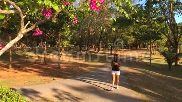 年轻的高加索女孩在公园里散步和使用智能手机慢镜头高清Stadicam镜头视频的预览图