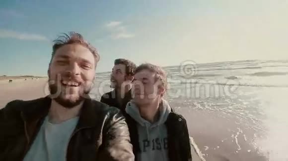 三个年轻的帅哥正站在一个美丽的沙滩上试图自拍视频的预览图