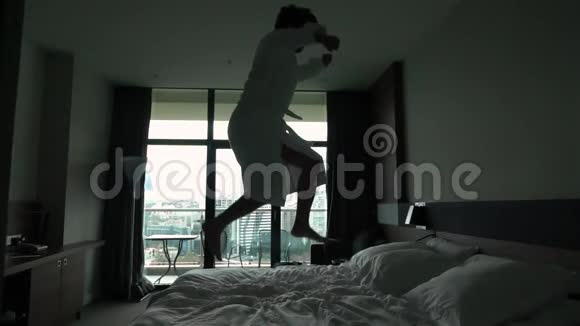 快乐的年轻人穿着浴袍在酒店的床上跳跃视频的预览图