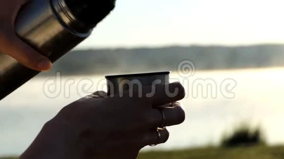 日落时分热水倒在湖岸上的烧瓶杯里视频的预览图