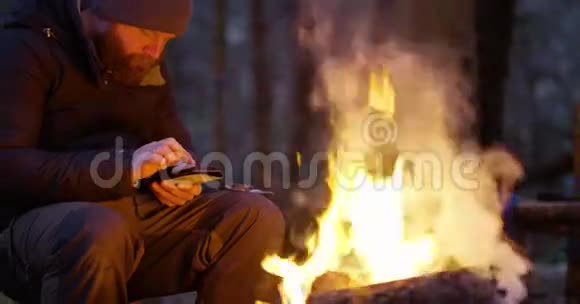 一个人在森林里篝火旁用罗盘和智能手机视频的预览图
