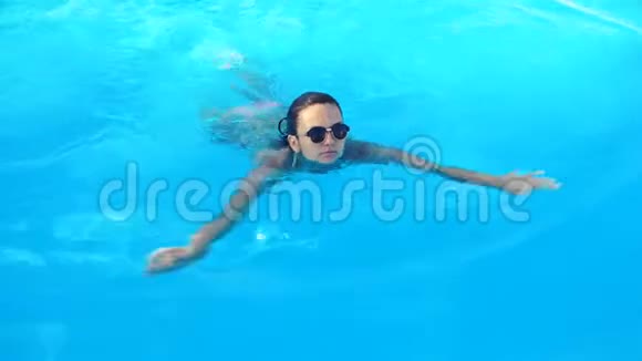 阳光明媚的夏日身着比基尼和太阳镜的年轻黑发女子在游泳池游泳视频的预览图