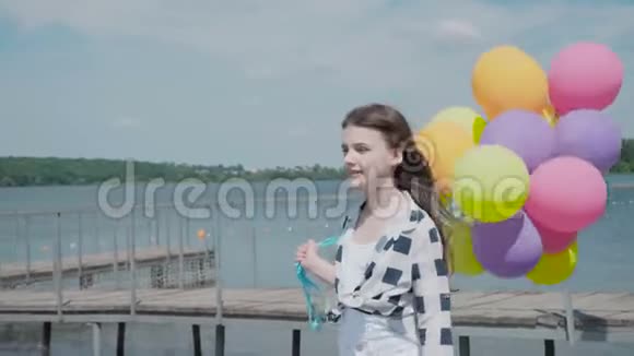 快乐的小女孩在夏天的海湾上摆着五颜六色的气球视频的预览图
