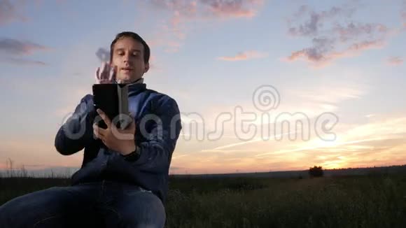 一个年轻人坐在夕阳下在平板电脑上的视频通话中交谈后面是美丽的天空视频的预览图