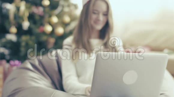 戴着圣诞帽的微笑女孩用手提电脑放在软椅上视频的预览图
