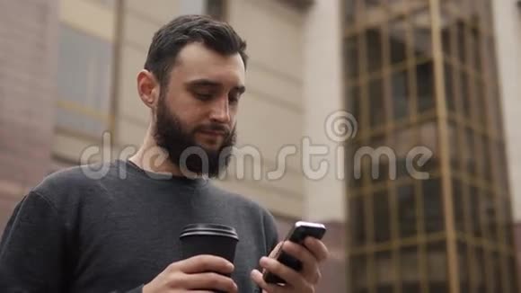 快乐的胡子年轻人在智能手机上聊天在日落时在街上喝咖啡视频的预览图