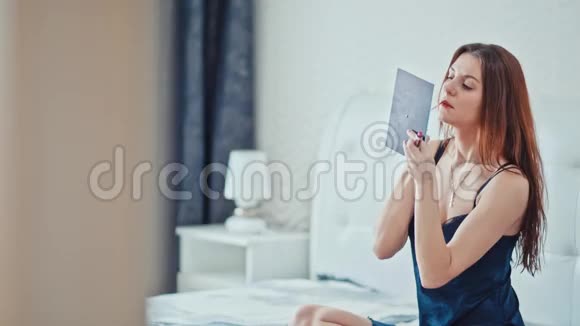 一个年轻漂亮的女孩坐在卧室的床上画着她的嘴唇视频的预览图