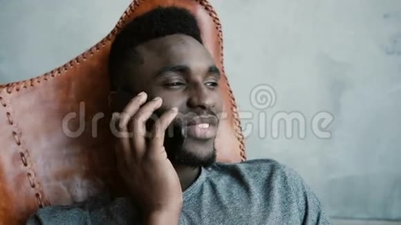 非洲年轻男性坐在椅子上用智能手机说话的肖像男人笑着点头同意视频的预览图