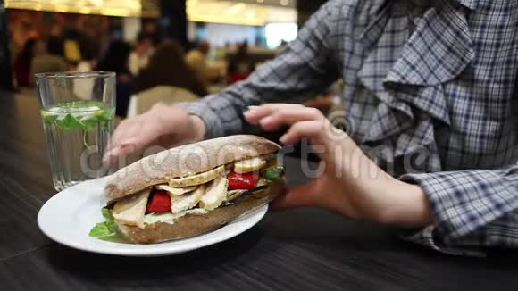 夹着鸡肉和蔬菜的三明治在盘子里在咖啡馆吃饭的女人的特写视频的预览图