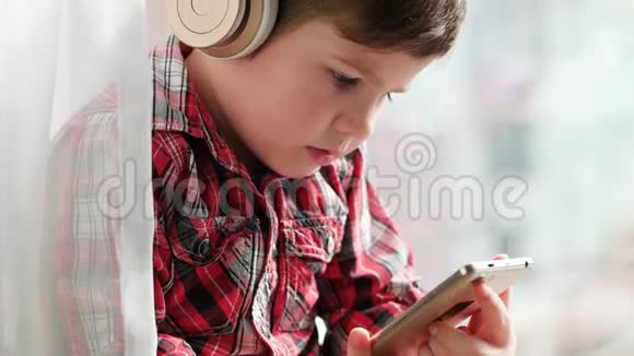 戴着智能手机耳机的男孩穿着衬衫看动画片的小孩视频的预览图