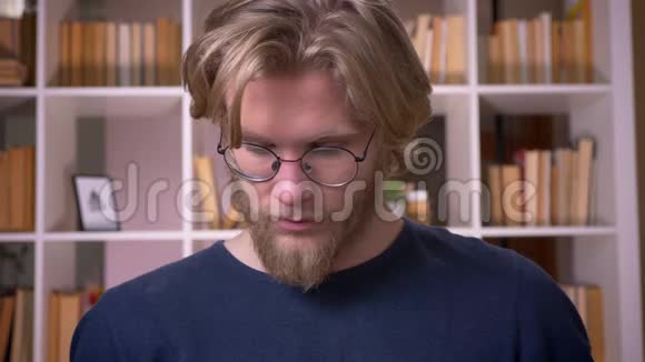 室内大学图书馆里戴眼镜看镜头的成年男生特写镜头视频的预览图
