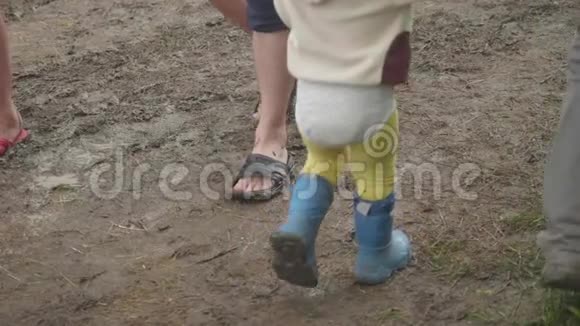 穿着橡胶靴的成人和蹒跚学步的孩子的腿在泥地中相互行走视频的预览图