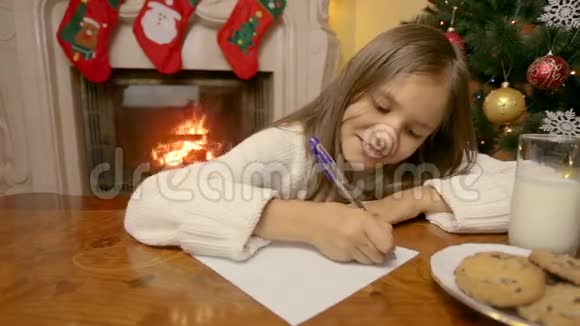 在壁炉旁的客厅里一个穿着白色毛衣的可爱女孩在给圣诞老人写信视频的预览图