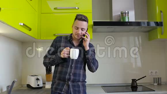 年轻人在家里的厨房里打电话和喝咖啡视频的预览图