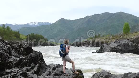 一个背着背包的女孩站在一条山河的岸边视频的预览图