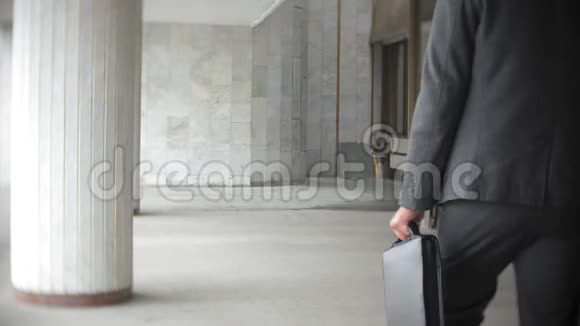 商人一边走一边提着公文包穿正装的男士在现代办公大楼附近散步视频的预览图
