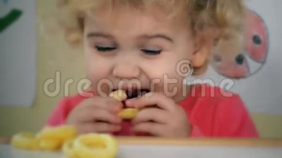 小女孩吃玉米圈坐在桌子旁边有玩具和图画在墙上视频的预览图