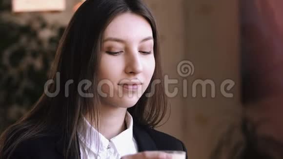 年轻女子喝着卡布奇诺或带牛奶的茶对着镜头微笑视频的预览图
