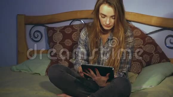 可爱的女孩坐在床上看着一台数码平板电脑视频的预览图