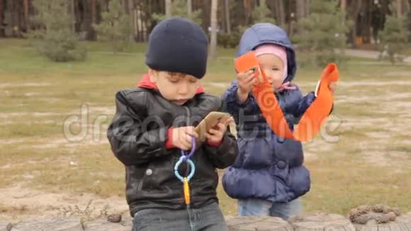 一个一岁的女孩在试一条宽阔的橙色腰带一个三岁的男孩坐在智能手机旁边按按钮视频的预览图