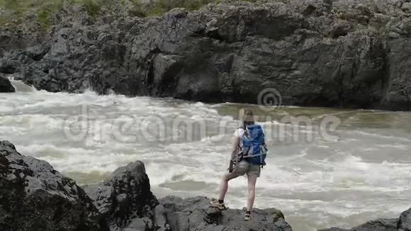 一个背着背包的女孩站在一条山河的岸边视频的预览图