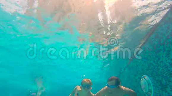 慢动作水下拍摄的父亲和他蹒跚学步的儿子在游泳池里游泳和玩耍视频的预览图