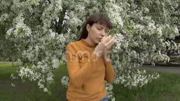 一个年轻的女人在一棵盛开的苹果树旁边打电话视频的预览图