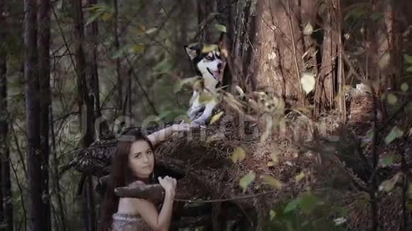 神秘的女人穿着毛皮上衣和她忠诚的狗站在森林里视频的预览图