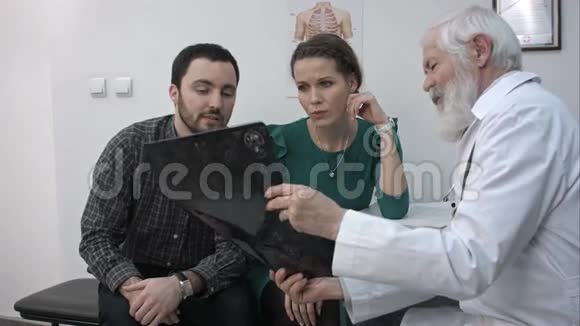 男高级医生在办公室里给一对夫妇看X光视频的预览图