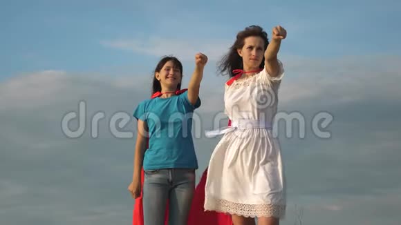 团队合作超级英雄两个穿着超级英雄红色斗篷的女孩站在蓝天上风吹着斗篷妈妈视频的预览图
