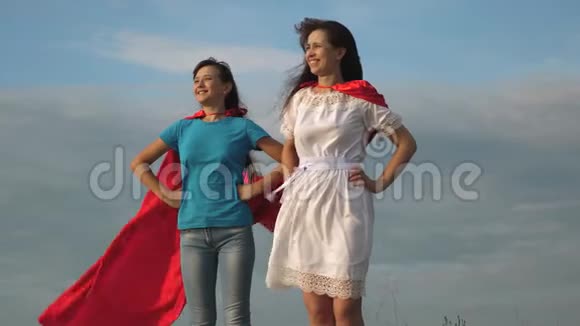 两个穿着超级英雄红色斗篷的女孩站在蓝天上风吹着斗篷妈妈和女儿玩视频的预览图