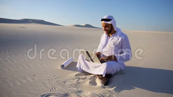 在炎热的夏天穆斯林阿拉伯阿联酋谢赫建筑师坐在沙漠上的沙子上视频的预览图