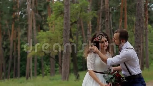奢华幸福的新娘和时尚的新郎坐在夏日森林的原木上新郎轻轻抚摸新娘视频的预览图