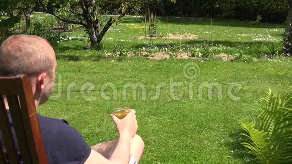 放松的男人在花园里坐在木椅上喝着玻璃啤酒4K视频的预览图